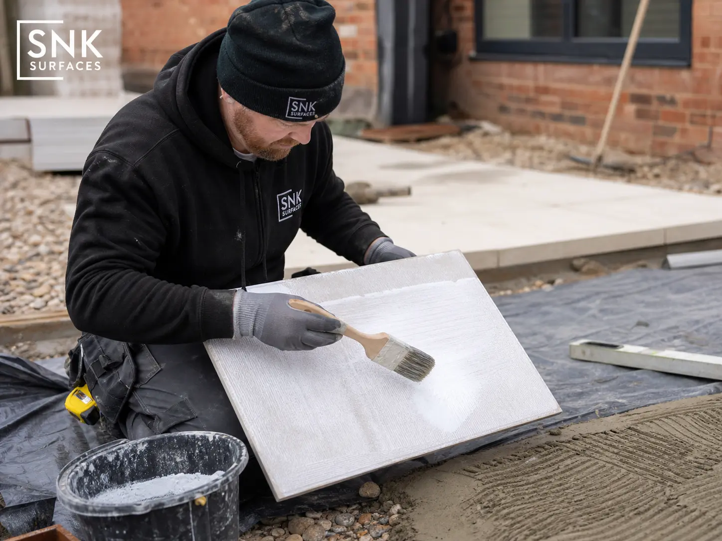 UK contractor applying SBR slurry primer to the reverse of a Quartz White Porcelain Paving tile