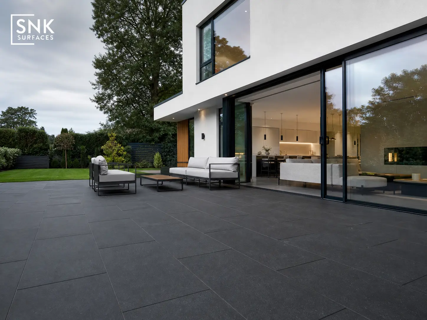 Modern UK new-build garden with large format Sagar Black Sandstone slabs and white-rendered house