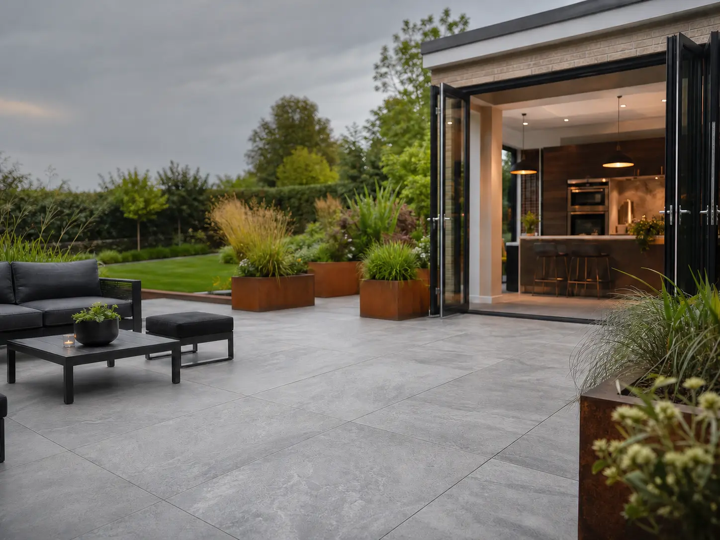 Luxury UK garden patio laid with large format kandla grey porcelain paving slabs and black bi-fold doors